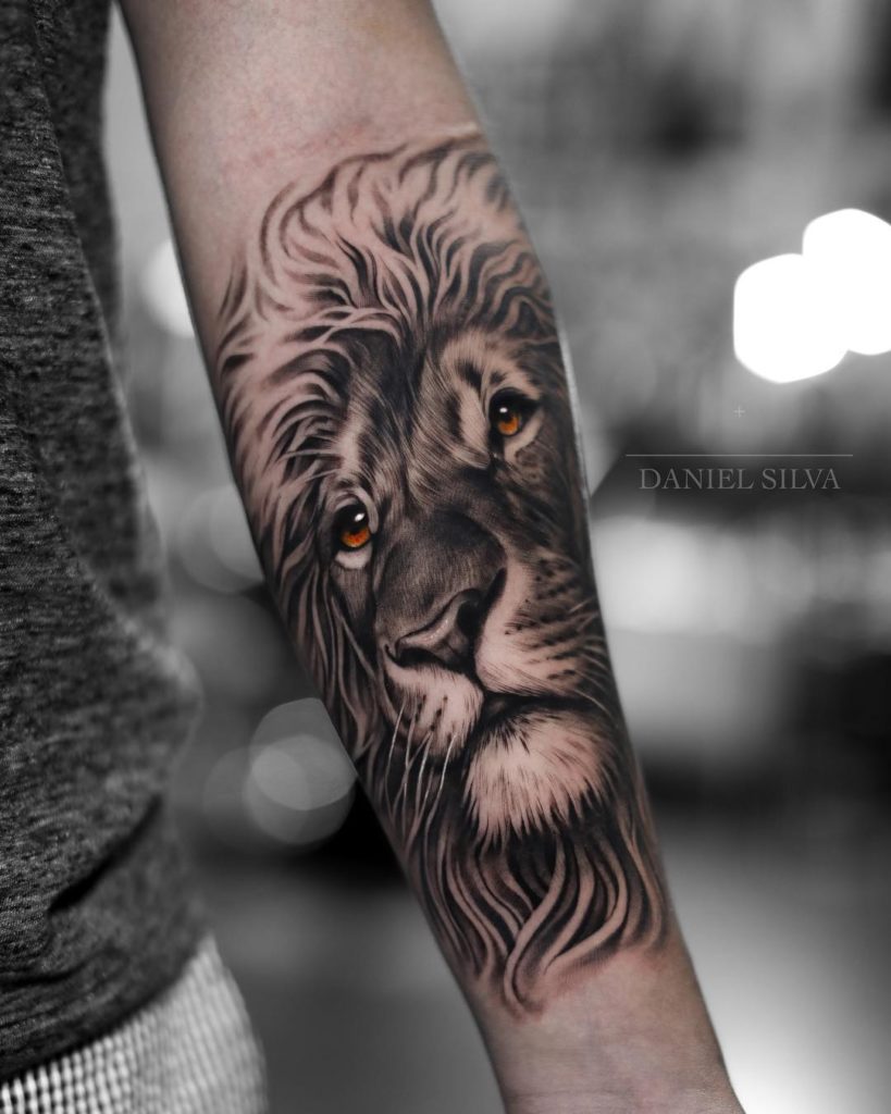 Graficzny Tatuaż głowa lwa na przedramieniu z pomarańczowymi oczami