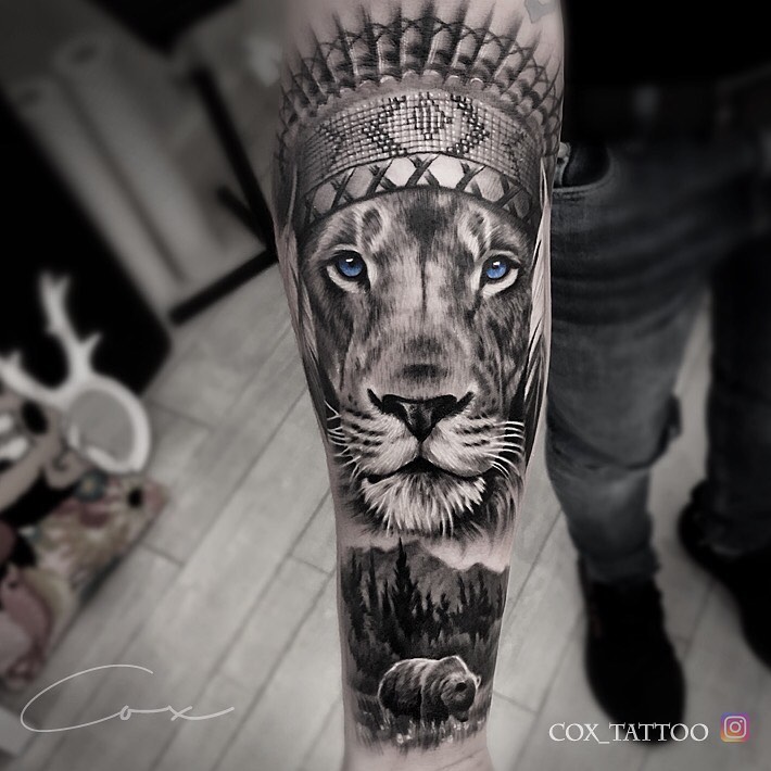 Tatuaż głowa lwa z piórami z niebieskimi oczami i niedźwiedziem i lasem Znaczenie dla mężczyzn i kobiet