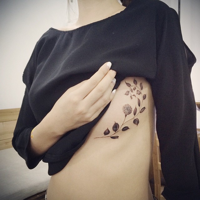 Tatuaż pod biustem, piersiami kobiece gałązką z listkami kolorowymi