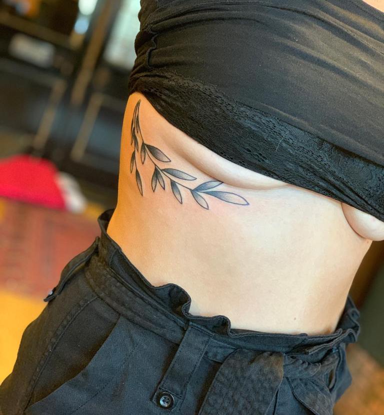 Tatuaż pod biustem, piersiami kobiece gałązka z listkami