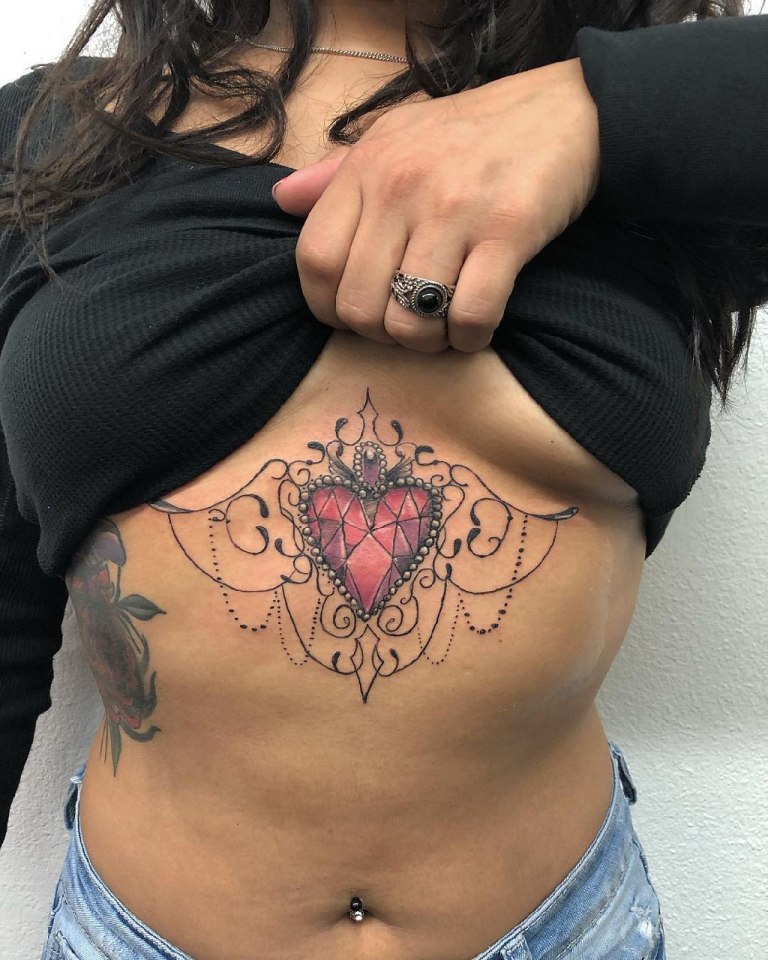 Tatuaż pod biustem, piersiami kobiece kolorowe serce z biżuteria